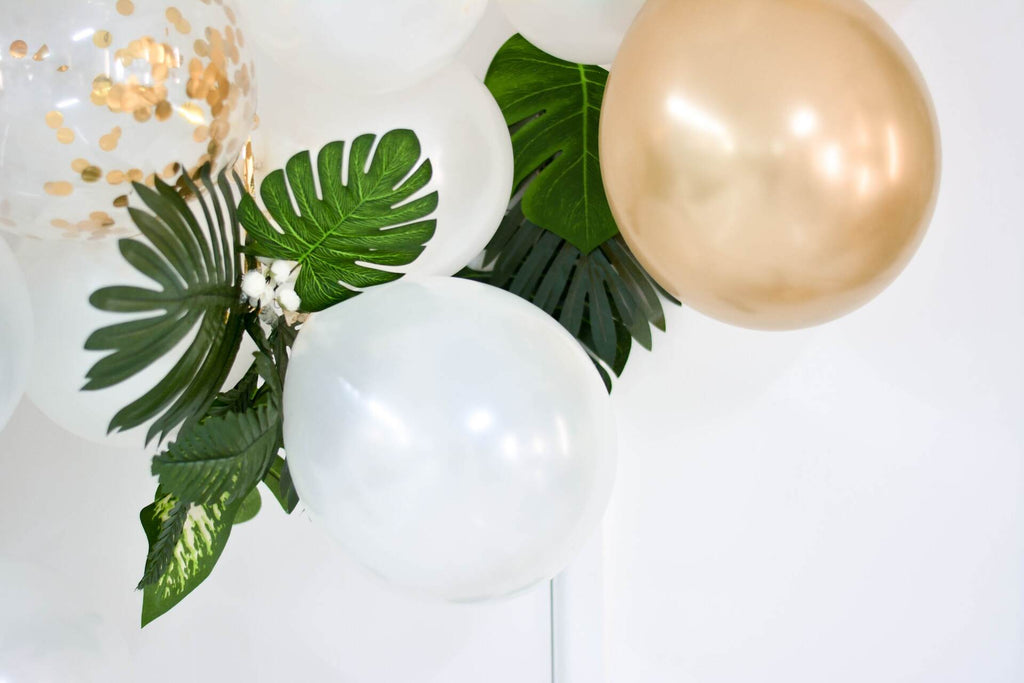 Gold and white balloon decor with tropical greenery