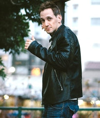 A mid-shot of author RJK Lee outdoors and looking at the camera, he is a white man with dark hair wearing a black leather jacket and jeans