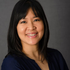 A smiling formal photograph of writer Geneve Flynn, an Australian-Asian author with long black hair and wearing a black shirt