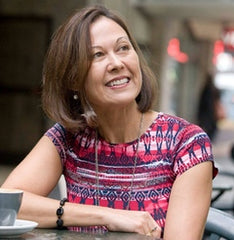 Author Lee Murray, sits at a table during a bright day, her dark hair and white skin are highlighted by a colourful shirt and smile