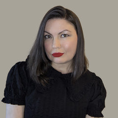 Formal image of author and editor Katya de Becerra, she is a dark-haired, pale-skinned woman looking at the camera, her lipstick is vibrant red, her shift is black