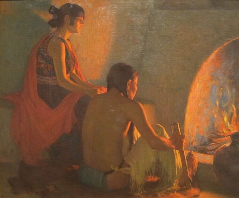 A young Pueblo Native man and woman sit side by side in contemplation of a glowing fire in an adobe hearth