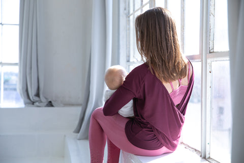 A new mom is breastfeeding her baby in sweat and milk's oceane 3 nursing sports bra