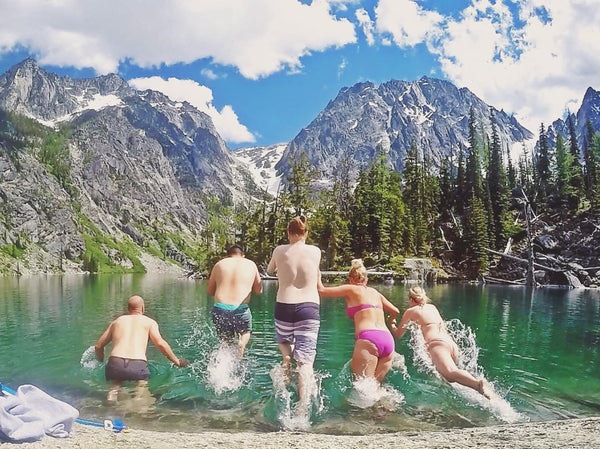 Five people running and jumping into icy water glacier runoff