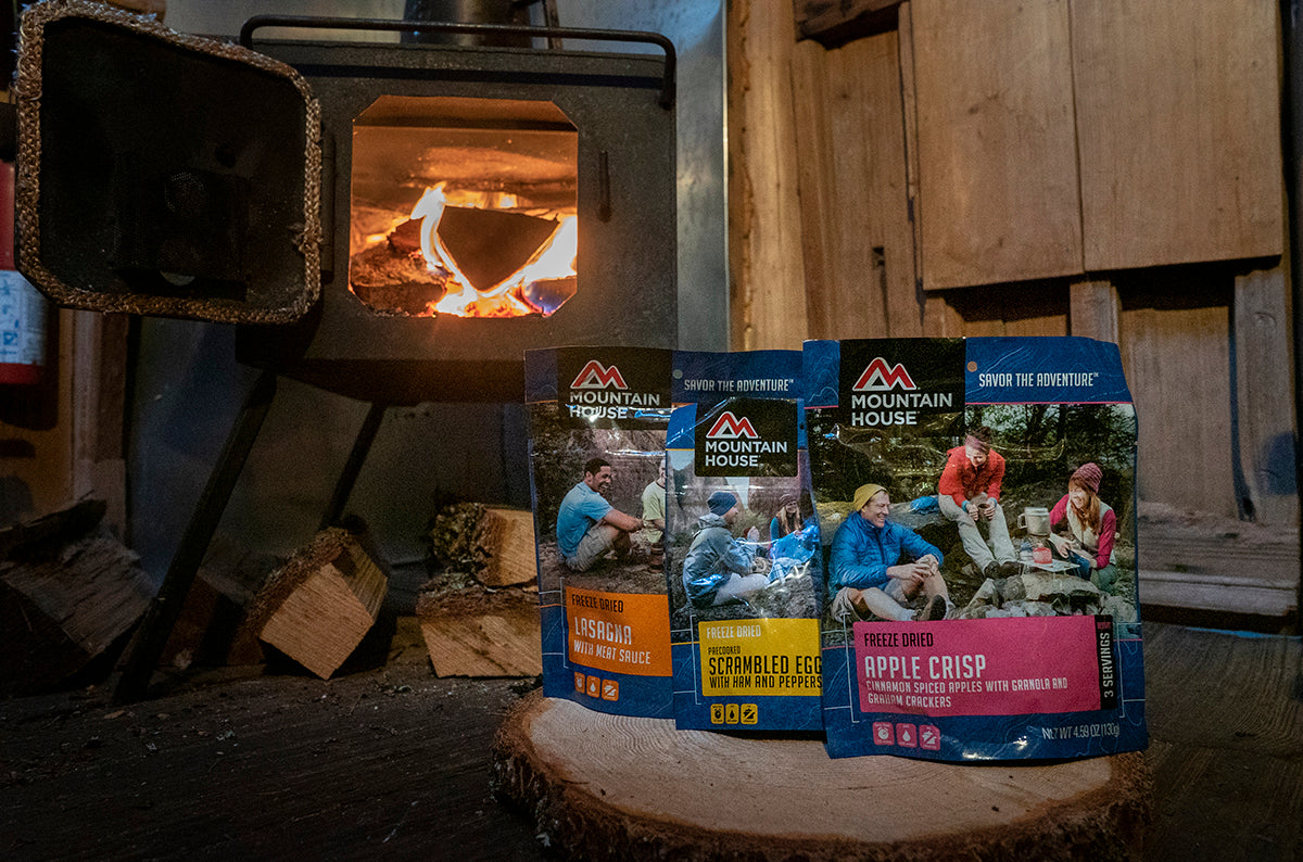 three mountain house pouches on stump on cabin floor in front of open wood stove