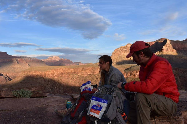 Couple sitting on plateau in colder weather with Mountain House meals