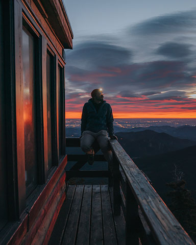 Person sitting on railing of lookout tower with headlamp staring at the sunset