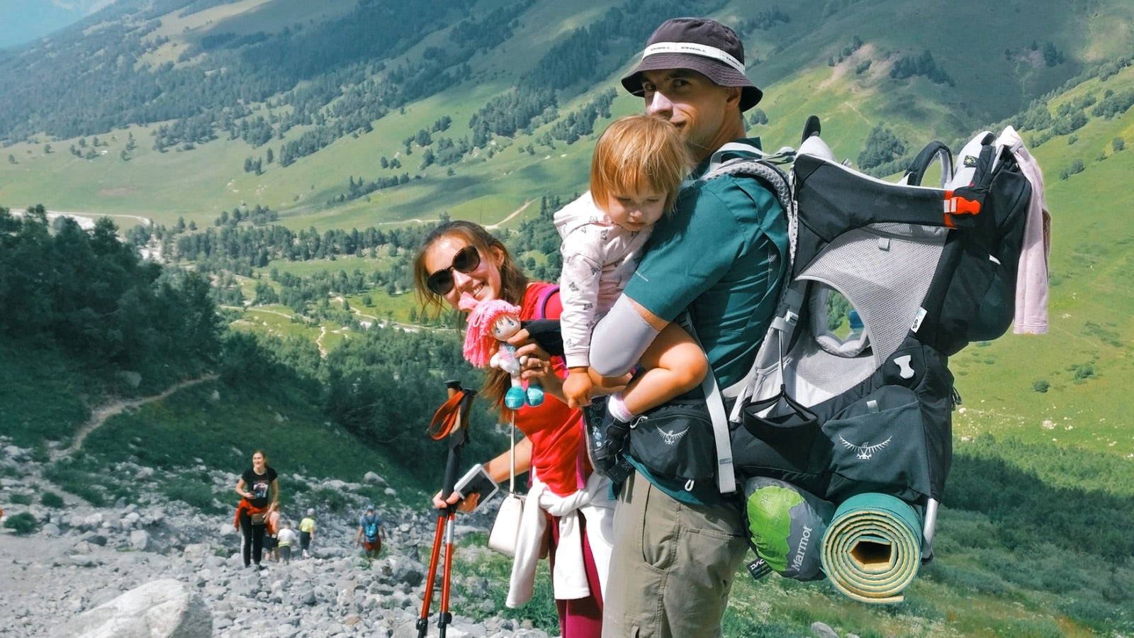 Man with large baby hiking carrier, carrying a little girls with a woman beside him