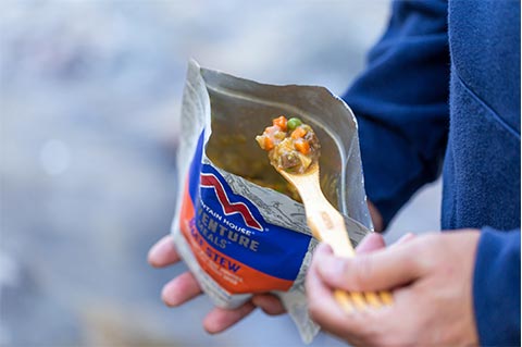 Person scooping out Beef Stew from Mountain House pouch on a wooden spork.