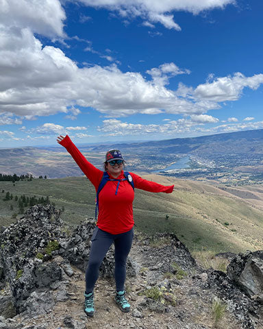 Doris on top of mountain peak with arms stretch wide in celebration