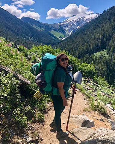 Mountain House Ambassador Doris on backpacking trail with thru-hike pack and shovel in hand