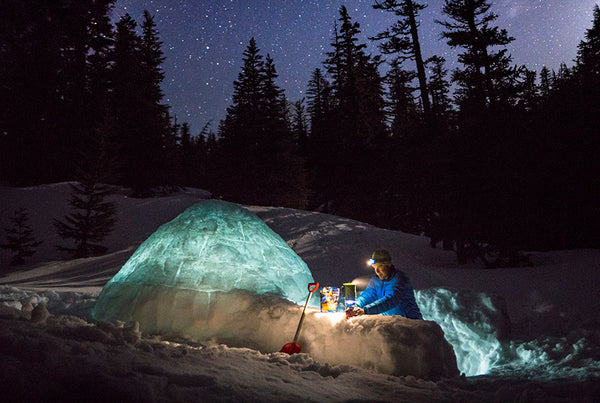Man with headlamp on building igloo shelter deep in snow