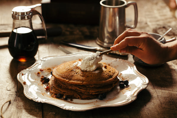 person putting butter on stack of pancakes