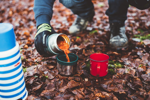 Hiker pours soup from thermos into camping mugs.