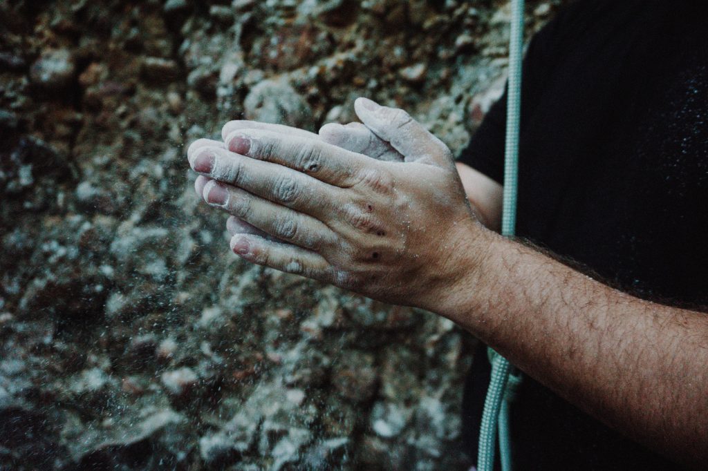 person holding climbing rope rubbing powder on hands