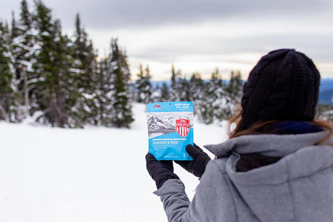 Girl holding up Chicken & Rice Pro-Pak pouch dressed in winter attire on snowy mountain