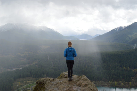 Woman hiker stands on rock overlooking mountain forest valley.