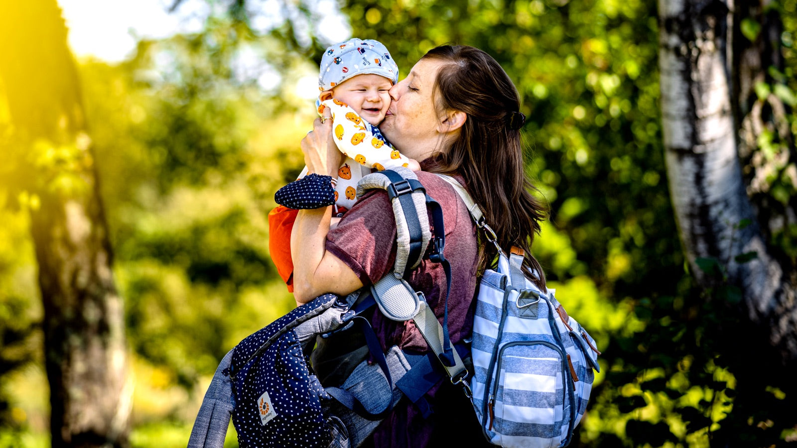 Woman kissing a baby while carrying baby hiking gear