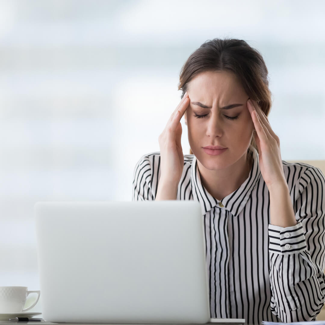 Une femme est assise devant un ordinateur portable et se tient la tête.