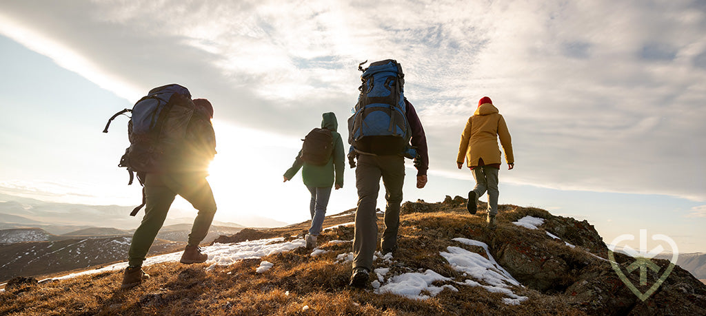Four people hiking with backpacks on a snowy mountain at sunset, picture taken from behind the group