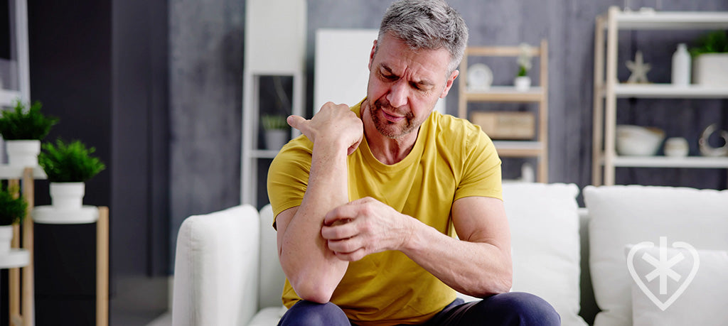 Man sitting on a sofa, visibly frustrated as he scratches at his forearm