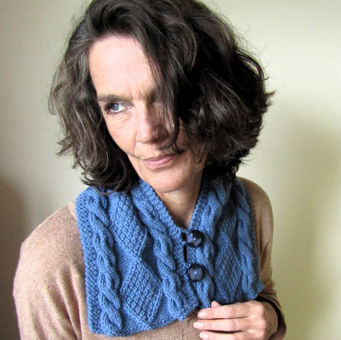 Dark Haired Thoughtful Lady Wearing An Unusual Blue Aran Chest and Neck Warmer With Two Black Buttons