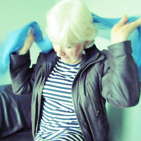 Blonde Lady Wearing a Black Leather Jacket and Stripey Dress Swirling A Mid Blue Silk Scarf Around Her Shoulders