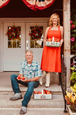 Wayne and Michelle Sirles of Rendleman Orchards sit on the Farm Market front porch and hold peaches.