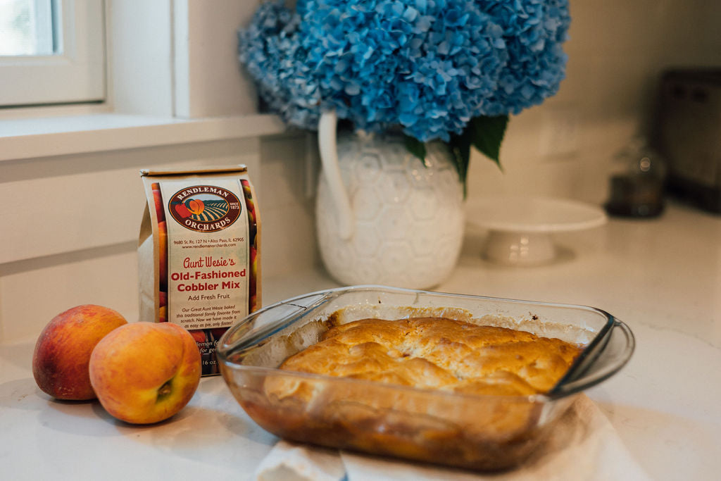 Rendleman Orchards old-fashioned peach cobbler mix pictured with a pan of homemade peach cobbler and two peaches.