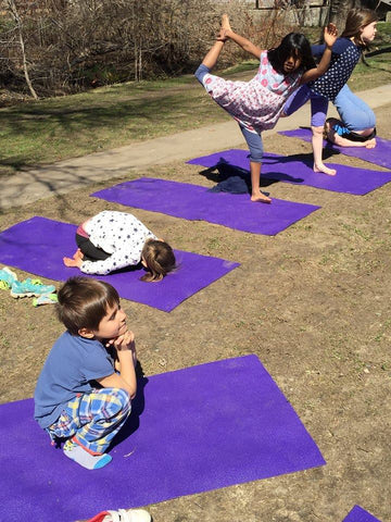Children doing yoga poses on purple mats outdoors in a semi circle on a sunny day