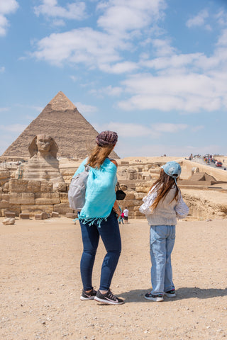 Mom and daughter standing in desert looking at pyramids