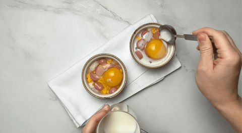 Pouring table cream over cheesy oeufs en cocotte