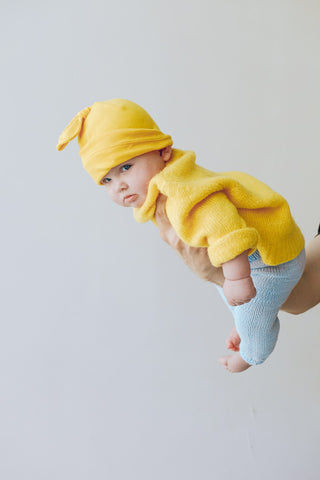 baby-wearing-yellow-sweater-and-hat-being-held-by-one-hand-first-year-of-motherhood.jpg