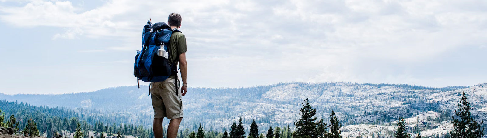 Man standing on hill looking out over pine trees and mountains