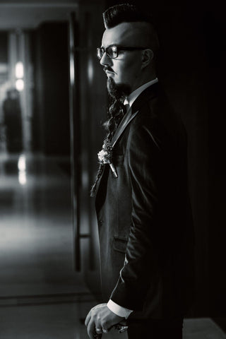 The groom in a tuxedo and bow tie with a mohawk hairstyle.