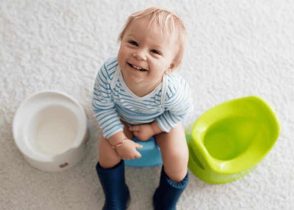 Young toddler boy sitting on top of his potty with a smiling face, there are two other potties on either side of him.