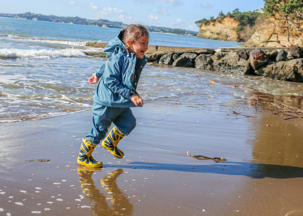 A young child playing on the beach in Brolly Sheets Wet Weather Gear in Denim