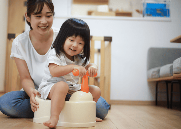 A little toddler playing on a potty that is shaped like a Bicycle with her mum in the lounge and kitchen area