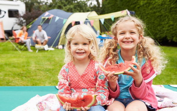 Two girls camping and eating watermelon with big smiles on their faces