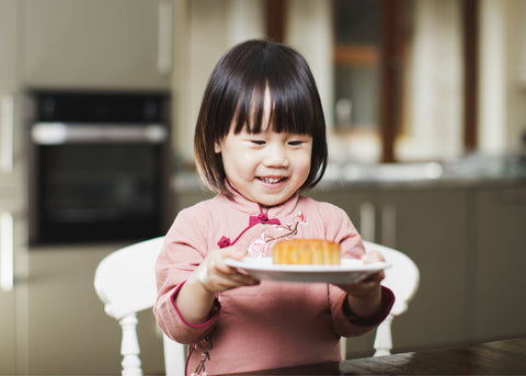 Little young female toddler excited holding a piece of cake she is going to eat