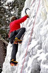 Man wearing a red jacket and gray pants climbing an ice wall with crampons