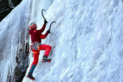 Woman in a colorful cold-weather outfit climbing a wall of ice with crampons