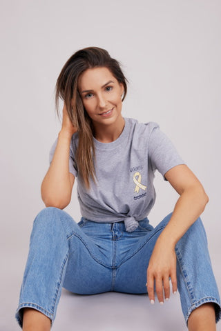 Aussie Battler founder Megan sits in a grey Aussie Battler shirt and jeans.