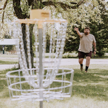 Man Throwing Disc Into Frisbee Golf Basket