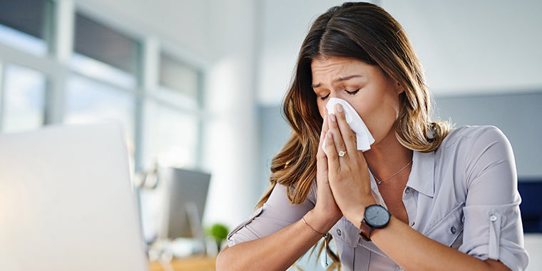 allergy relief from allergy medications image of woman blowing her nose from having allergies at work