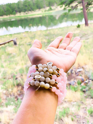 Wrist wearing a stack healing gemstone bead bracelets with rose quartz and moonstone.