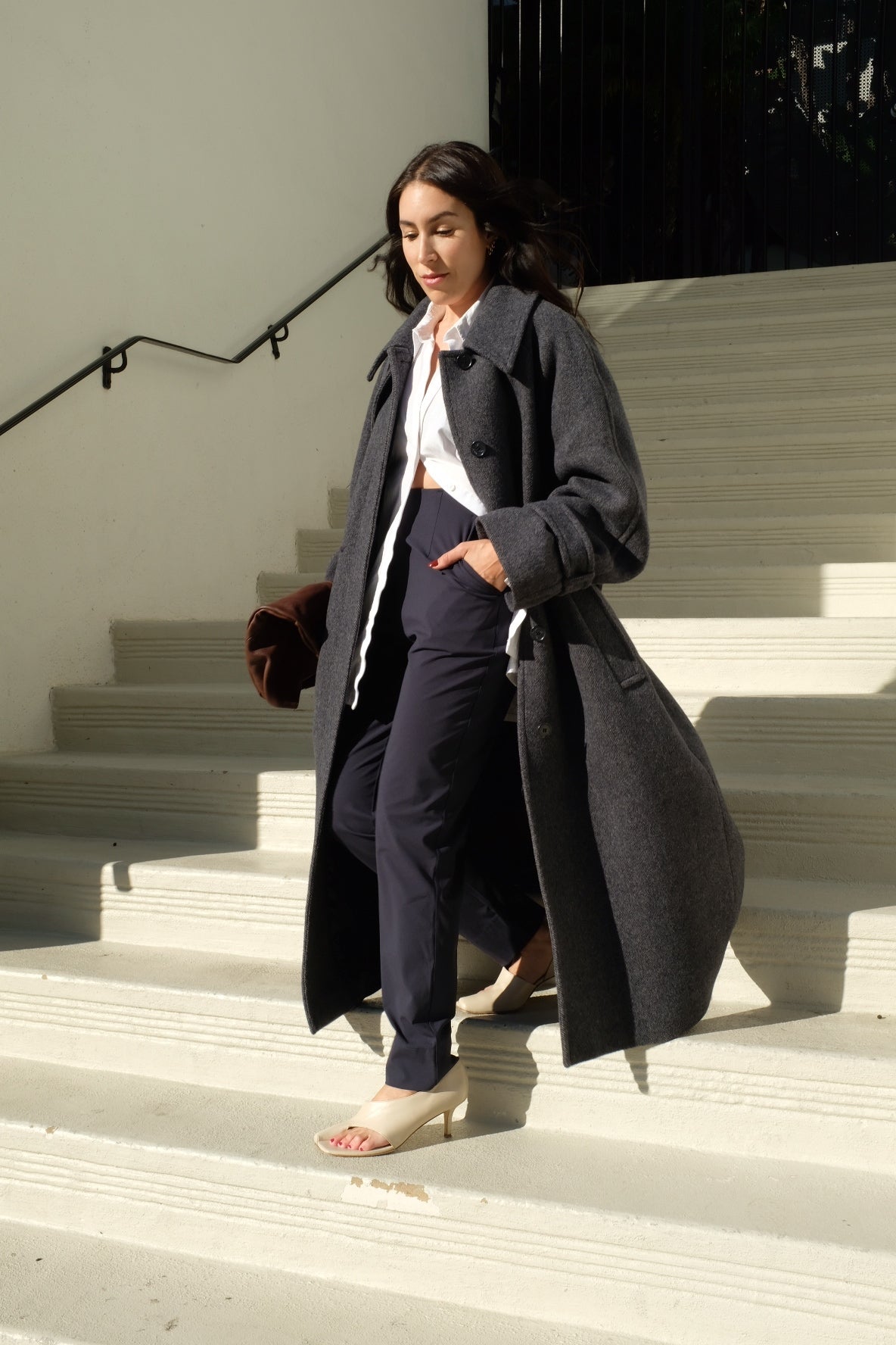 Woman descending stairs in stylish attire with a coat and heels.