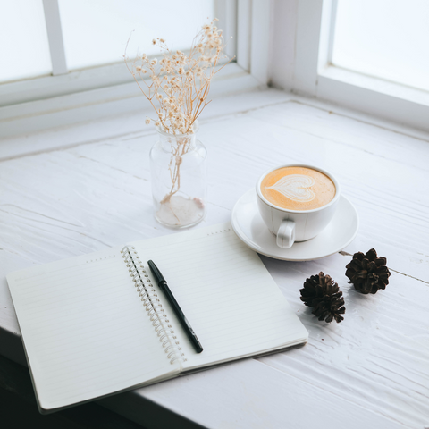 Journal with cup of coffee on white desk