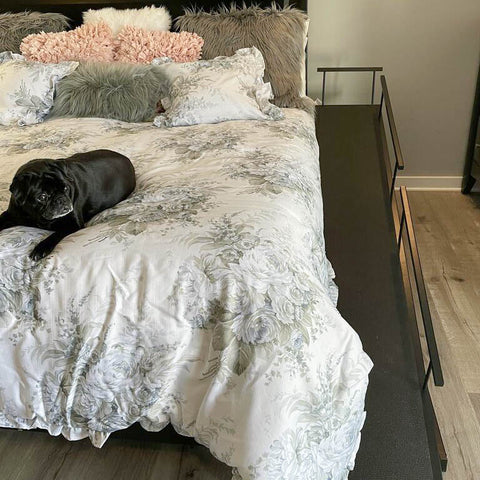A pug rests on her owner's bed with her DoggoRamps Bed Ramp for Small Dogs next to it