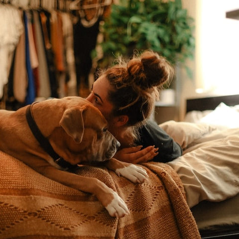 A dog owner snuggling her dog on her bed